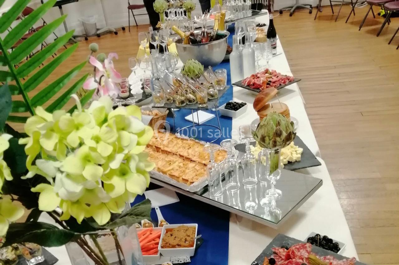 Table garnie de plats variés, charcuteries, fromages, verrines et boissons, décorée de fleurs et servie pour un événement.