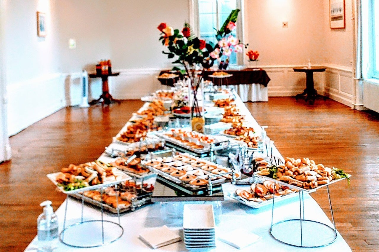 Table dressée avec un buffet varié de plats et amuse-bouches dans une grande salle lumineuse.