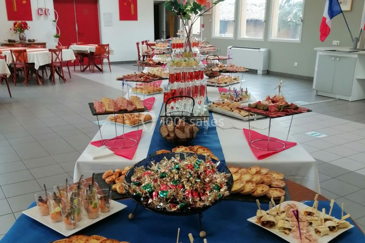 Buffet varié avec plats salés, verrines, desserts et décorations, disposé sur une longue table dans une salle lumineuse.