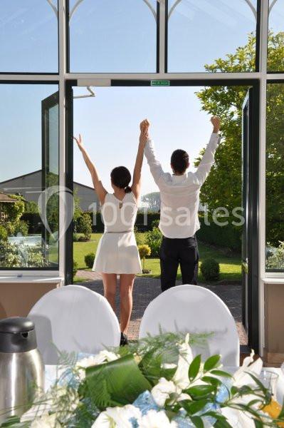 Un couple de dos, bras levés, se tient devant une porte ouverte donnant sur un jardin ensoleillé.