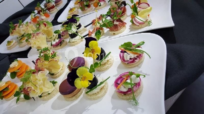 Assortiment de canapés colorés et décorés avec des fleurs comestibles et des garnitures variées sur des plateaux blancs.