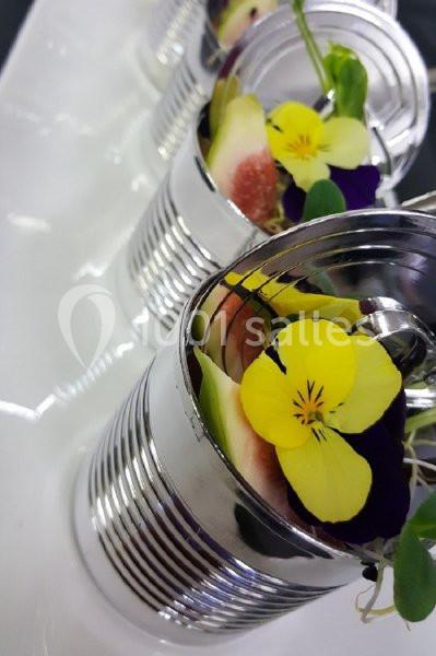 Des conserves métalliques ouvertes contenant des figues fraîches et des fleurs comestibles sur une assiette blanche.