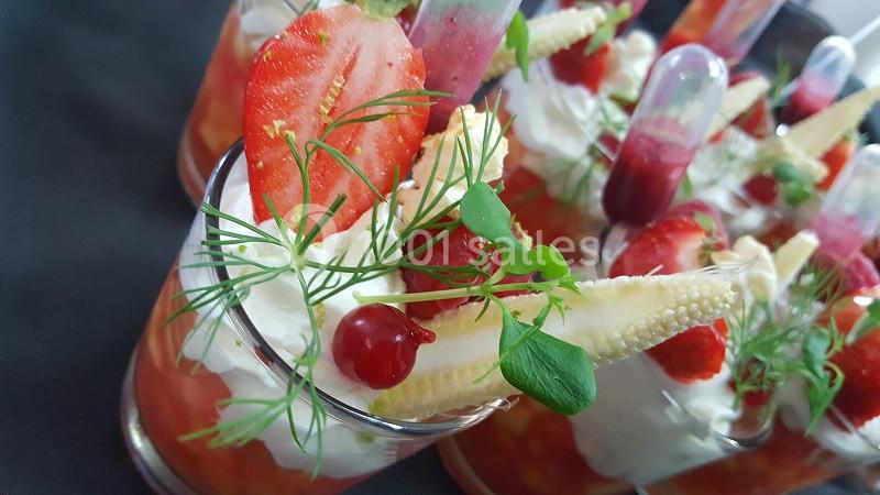 Verrines garnies de fraises, groseilles, maïs miniature, crème et pipettes de coulis, décorées d'herbes fraîches.
