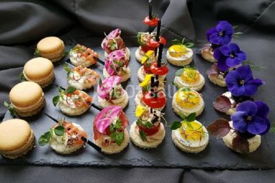 Plateau de bouchées apéritives variées avec macarons salés, canapés garnis et fleurs comestibles sur ardoise noire.