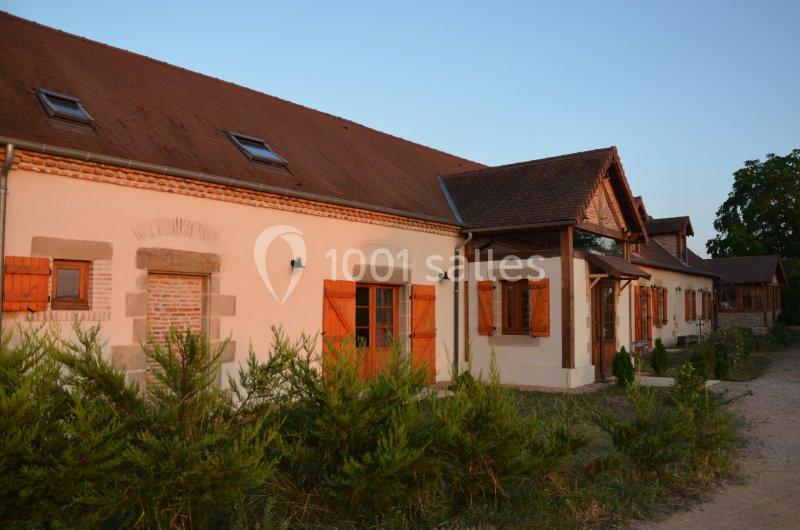 Façade d'une maison traditionnelle avec murs clairs, volets en bois et toit en tuiles, entourée de végétation.
