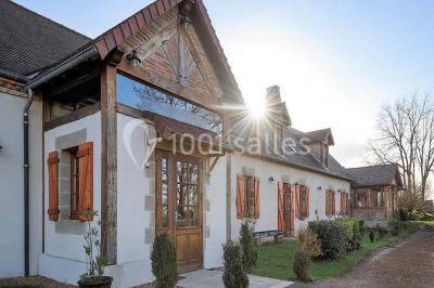 Façade d'une maison en briques et bois avec fenêtres à volets, entourée de végétation et baignée de lumière naturelle.