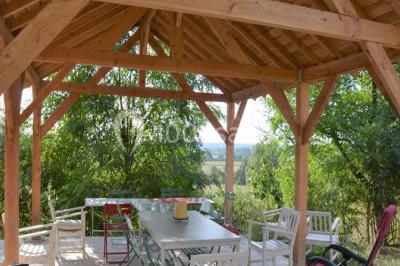 Façade d'une maison en briques et bois avec fenêtres à volets, entourée de végétation et baignée de lumière naturelle.