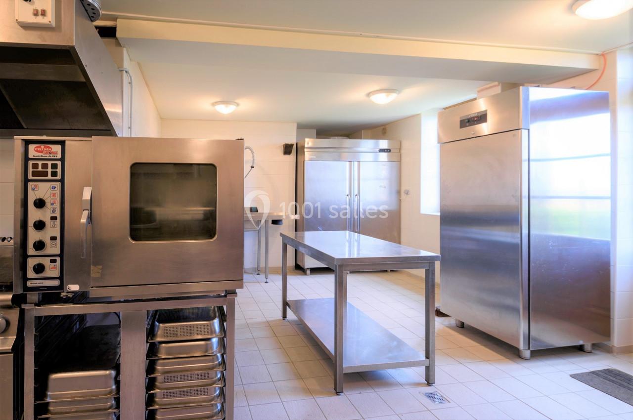 Cuisine professionnelle avec four, réfrigérateurs en inox, plans de travail métalliques et éclairage au plafond.