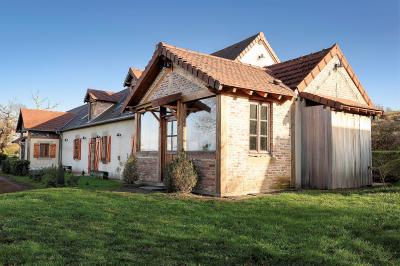 Façade d'une maison en briques et bois avec fenêtres à volets, entourée de végétation et baignée de lumière naturelle.