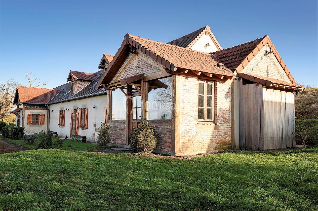Maison en briques et bois avec toit en tuiles, entourée de pelouse et située dans un cadre rural.