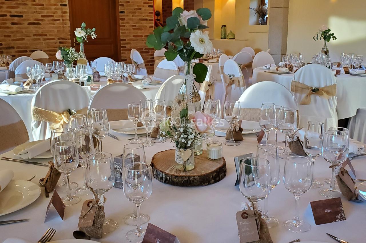 Salle de réception décorée avec des tables rondes élégantes, nappes blanches, fleurs et vaisselle raffinée.