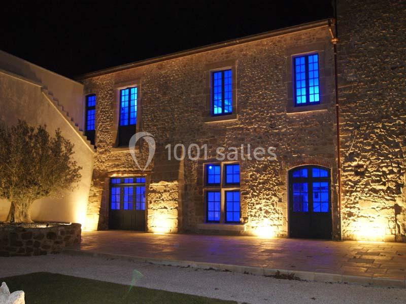 Façade en pierre d'un bâtiment éclairé par des lumières bleues et jaunes, vue de nuit.