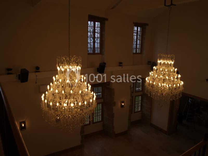 Deux grands lustres en cristal allumés suspendus dans une pièce avec de hautes fenêtres et des murs clairs.