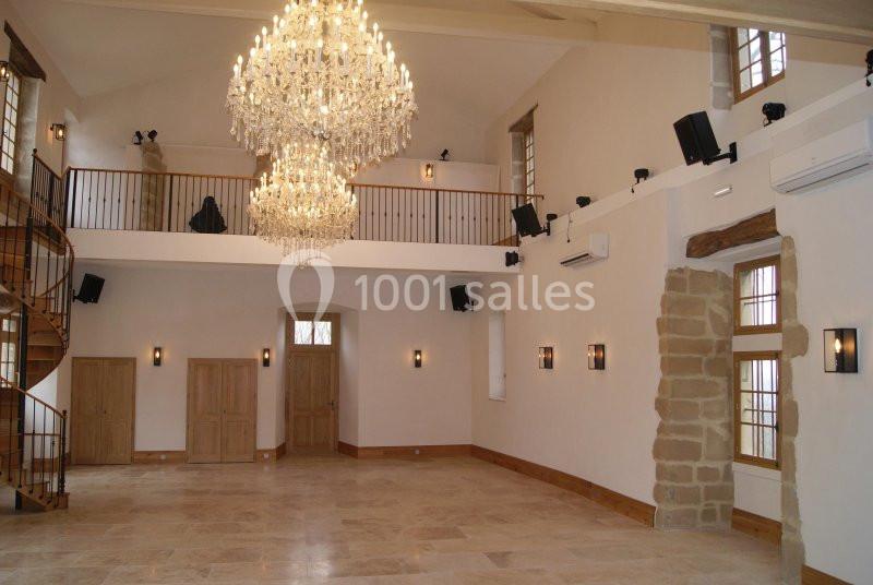 Salle spacieuse avec sol en pierre, lustres en cristal, mezzanine en bois et murs clairs ornés de fenêtres.