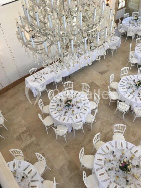Salle de réception élégante avec tables rondes dressées, nappes blanches et grand lustre en cristal.