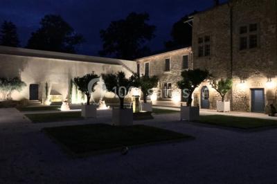 Allée éclairée par des lampes au sol, bordée d'arbres et menant à une entrée illuminée dans l'obscurité.