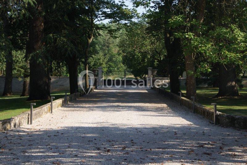 Allée gravillonnée bordée d'arbres menant à un portail fermé dans un cadre verdoyant.