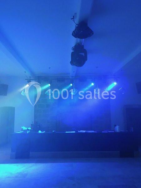 Salle de spectacle vide éclairée par des projecteurs bleus, avec une scène et des équipements suspendus au plafond.