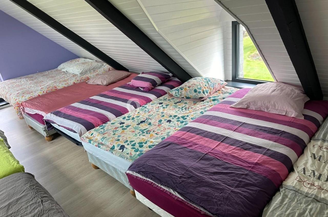 Quatre lits simples alignés sous un toit mansardé, avec des draps colorés et une fenêtre donnant sur un jardin.