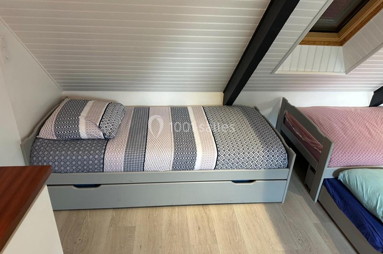 Lit simple avec tiroirs intégré, draps à motifs géométriques, situé sous un plafond mansardé avec fenêtre de toit.