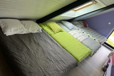 Chambre moderne avec mur vert, lit double décoré de coussins, luminaires muraux et tapis clair au sol.