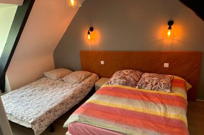 Chambre moderne avec mur vert, lit double décoré de coussins, luminaires muraux et tapis clair au sol.