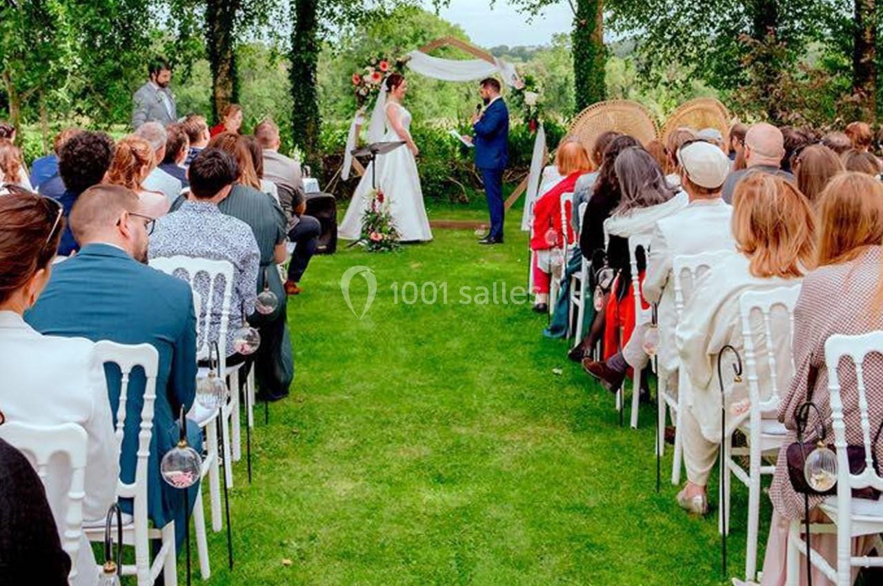 Cérémonie de mariage en plein air, avec des invités assis et un couple échangeant leurs vœux devant un décor floral.