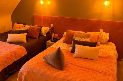 Chambre moderne avec mur vert, lit double décoré de coussins, luminaires muraux et tapis clair au sol.