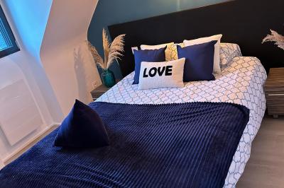 Chambre moderne avec mur vert, lit double décoré de coussins, luminaires muraux et tapis clair au sol.