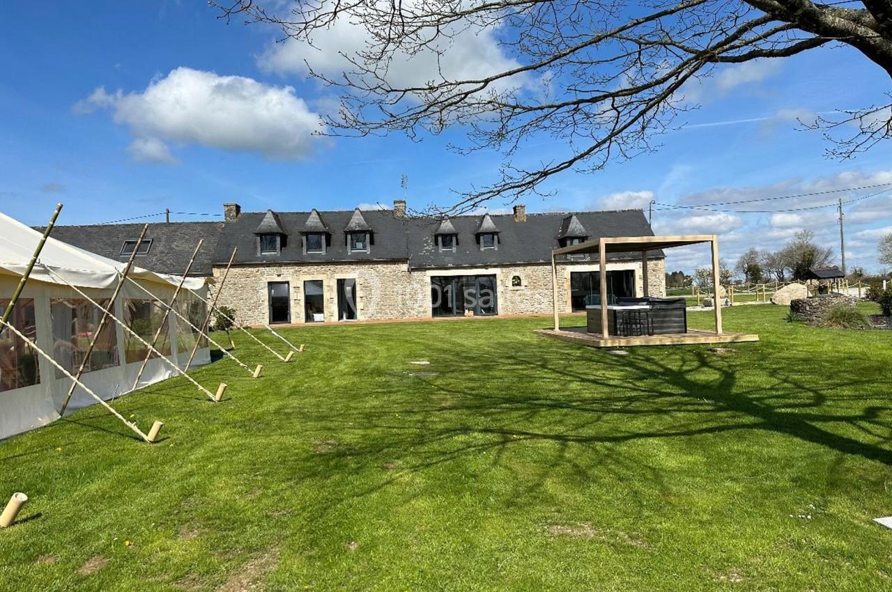 Grande maison en pierre avec toit en ardoise, entourée d'une pelouse, avec une terrasse et un jacuzzi extérieur.