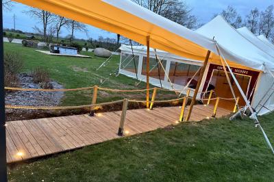 Chambre moderne avec mur vert, lit double décoré de coussins, luminaires muraux et tapis clair au sol.