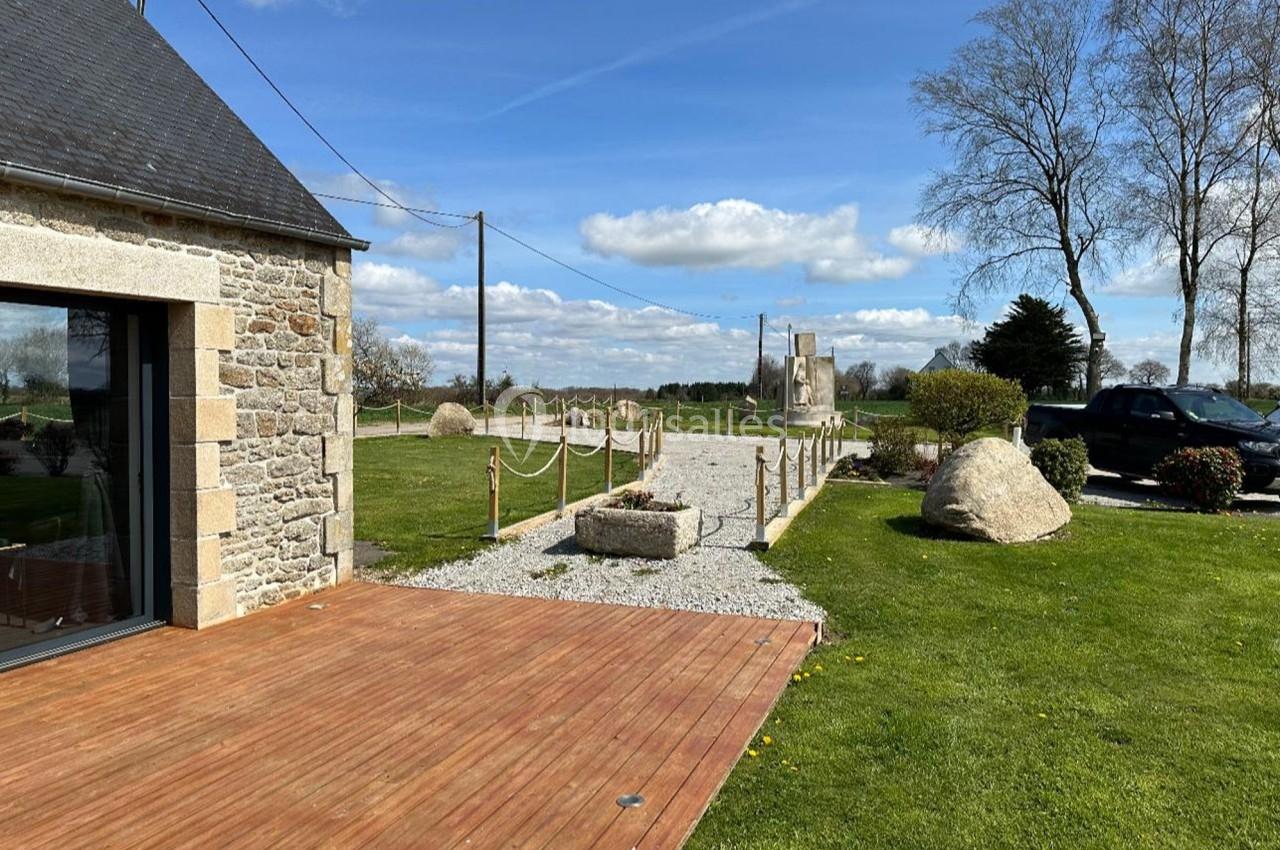 Allée en gravier bordée de poteaux en bois, menant à un jardin avec pelouse, arbres et rochers sous un ciel dégagé.