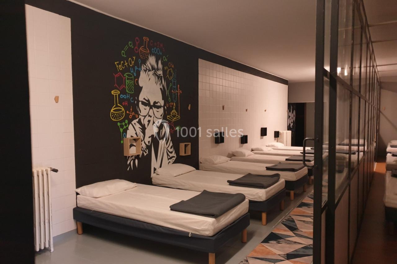 Dortoir moderne avec lits alignés, mur décoré d'une fresque colorée et cloison vitrée sur le côté.