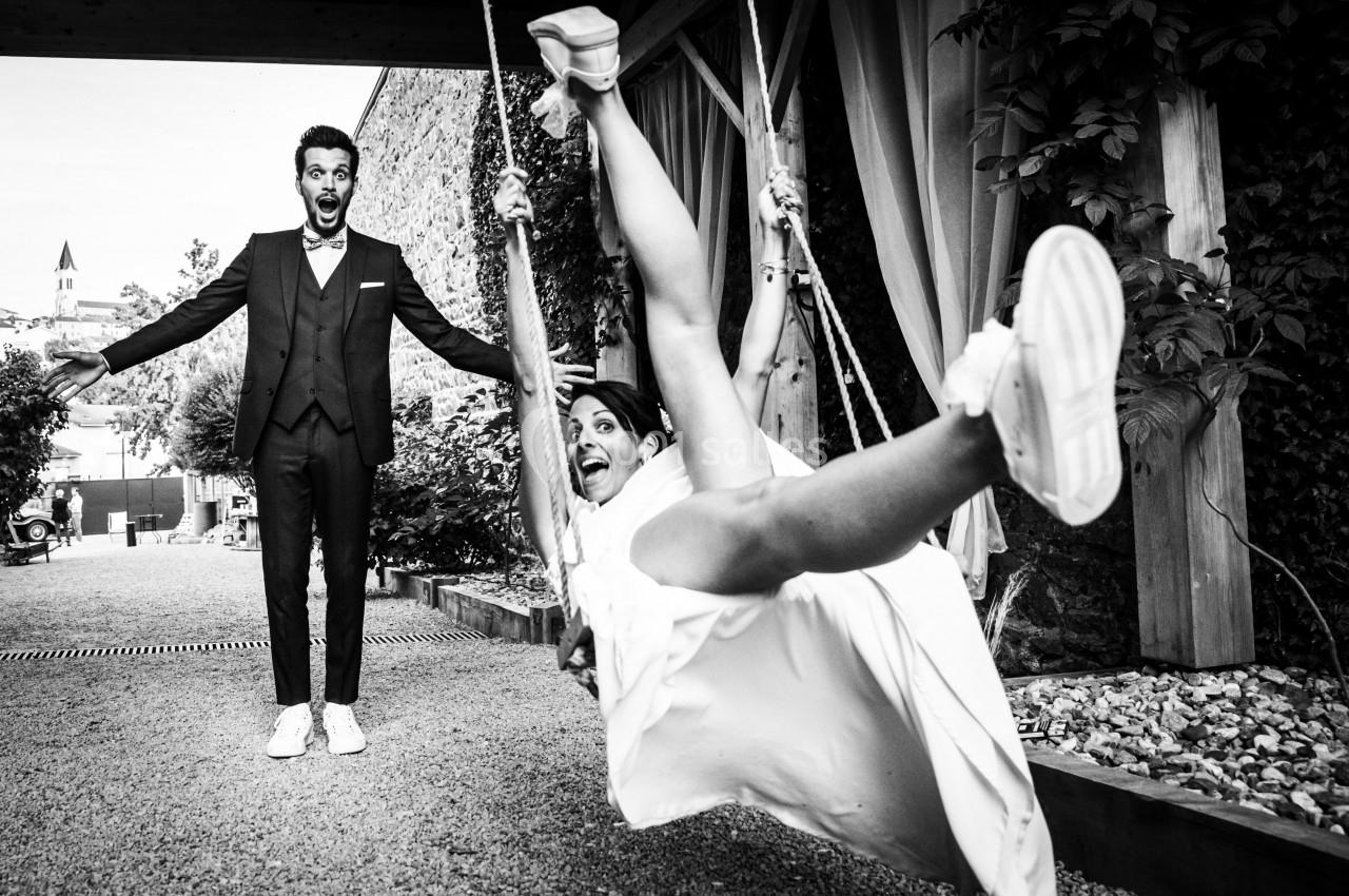 Un homme en costume surpris regarde une femme en robe blanche qui se balance joyeusement sur une balançoire.