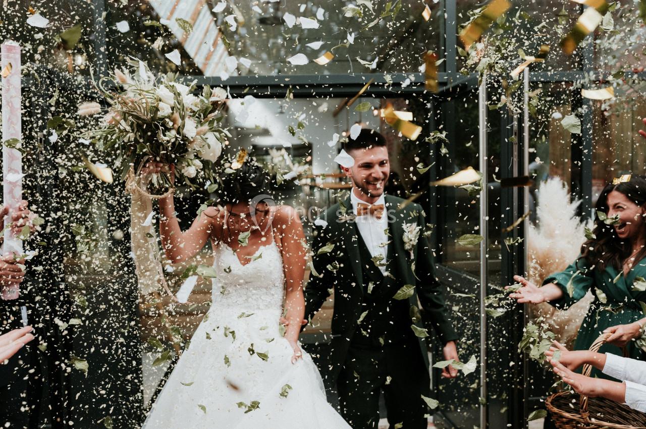 Un couple de mariés souriants sort sous une pluie de confettis, entouré d'invités célébrant leur union.