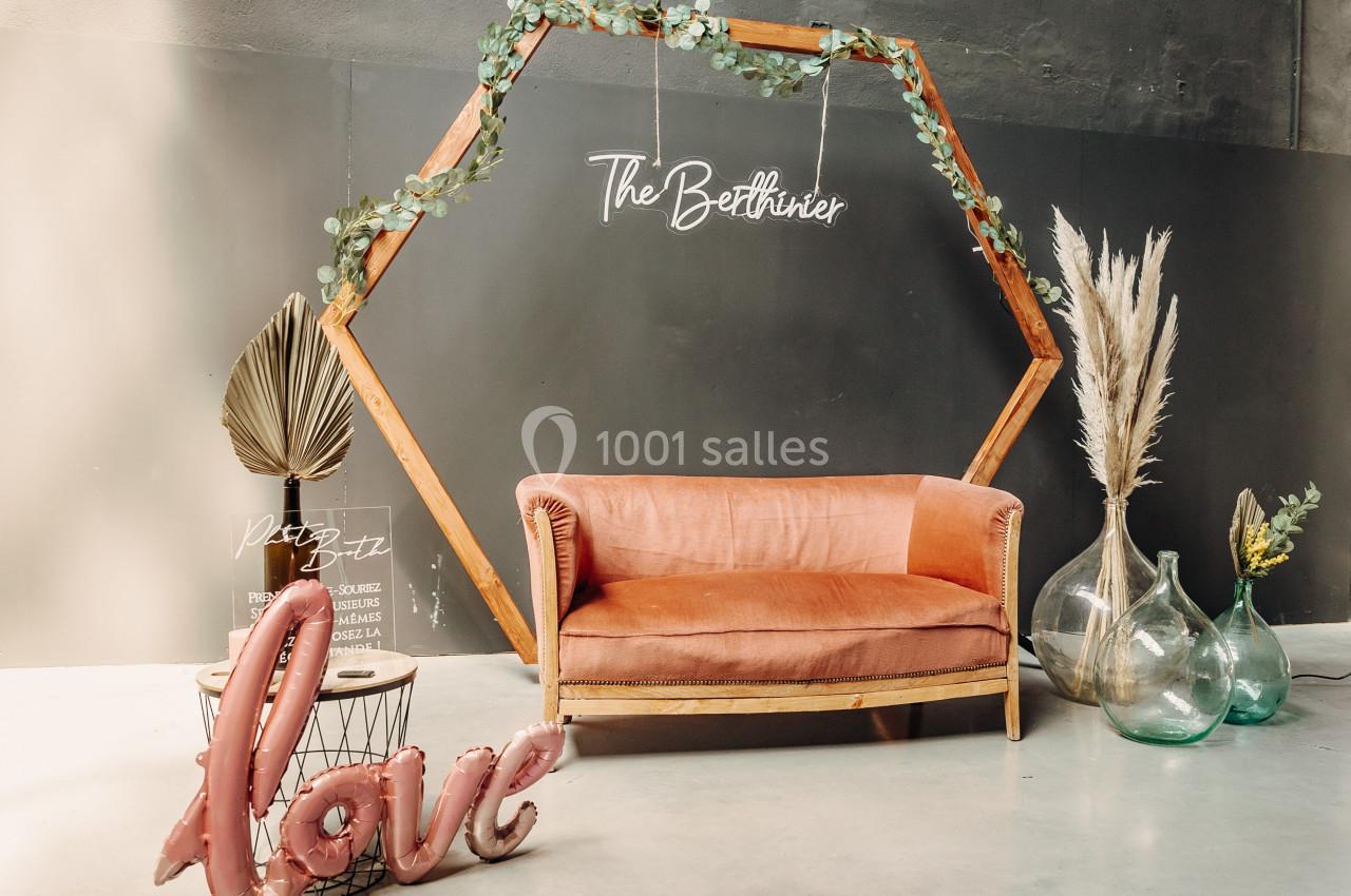 Canapé rose devant un cadre hexagonal en bois décoré de feuillage, avec des vases et des ballons formant le mot ’love’.