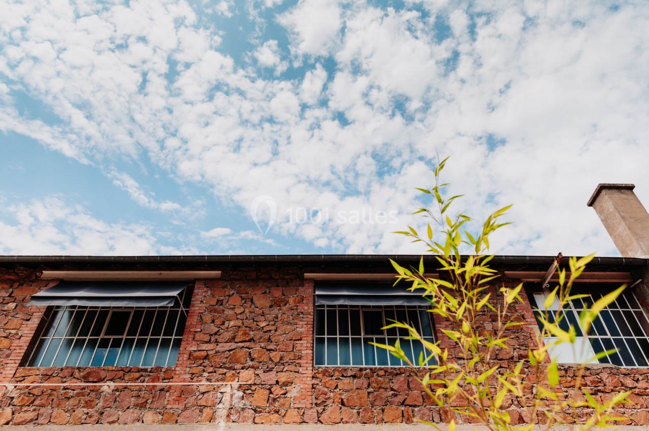 Façade en pierre d'un bâtiment avec fenêtres grillagées, ciel bleu nuageux et bambou au premier plan.