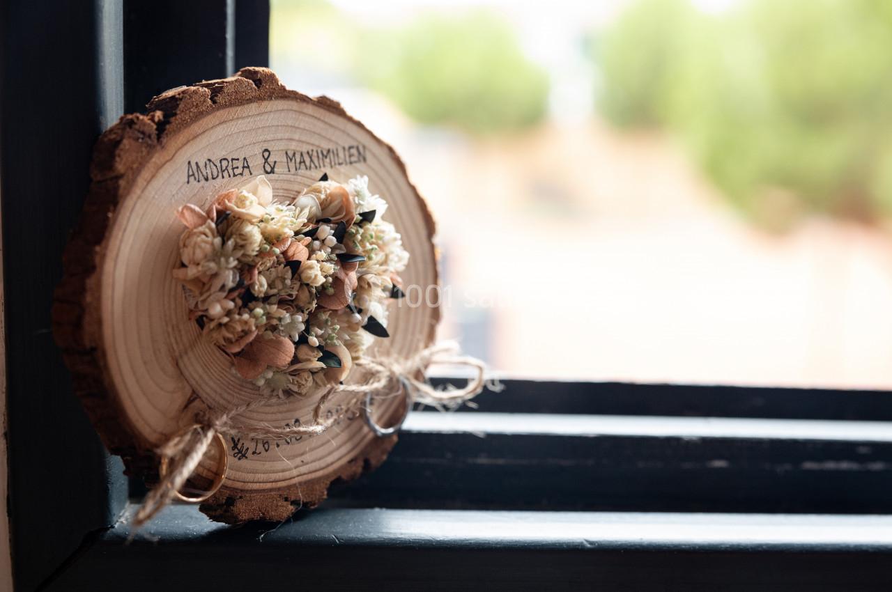 Tranche de bois gravée avec des prénoms, décorée de fleurs séchées, posée sur un rebord de fenêtre.