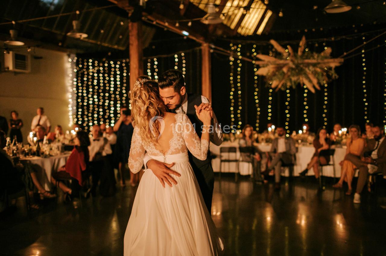 Un couple danse dans une salle décorée de guirlandes lumineuses, entouré d'invités assis à des tables.