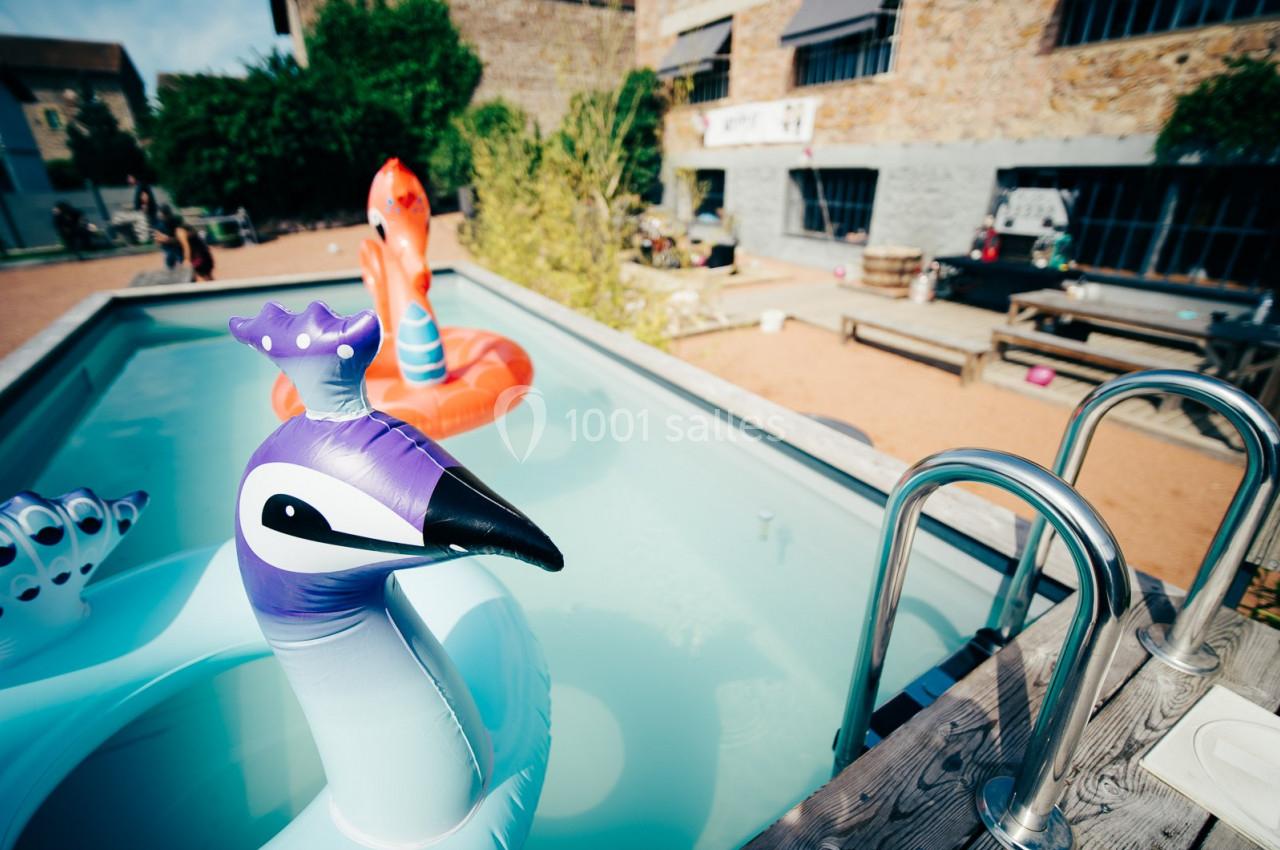 Bouée en forme de paon flottant dans une petite piscine extérieure, avec des bâtiments en arrière-plan.