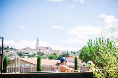 Des personnes se détendent dans une piscine extérieure avec vue sur un village et un clocher sous un ciel dégagé.