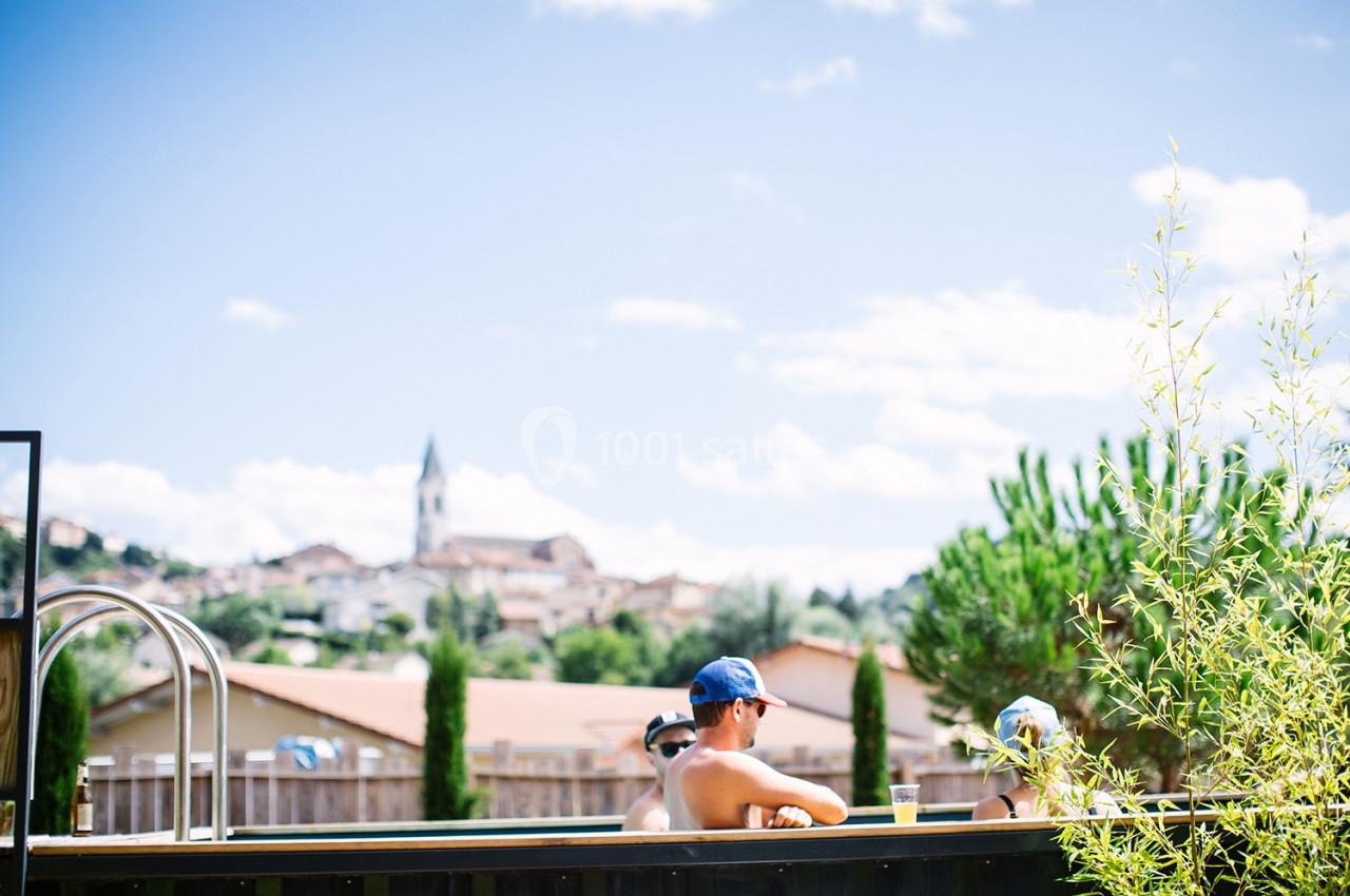 Des personnes se détendent dans une piscine extérieure avec vue sur un village et un clocher sous un ciel dégagé.