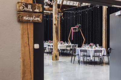 Salle lumineuse avec de grandes tables en bois dressées, chaises noires, décor minimaliste et verrière en hauteur.