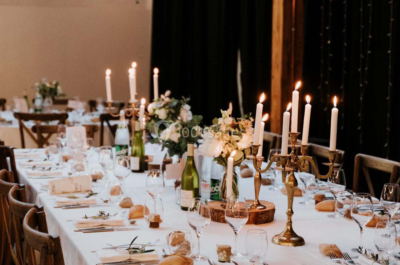 Table de réception élégamment dressée avec nappes blanches, chandeliers, fleurs et vaisselle raffinée.