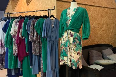 Salle lumineuse avec de grandes tables en bois dressées, chaises noires, décor minimaliste et verrière en hauteur.