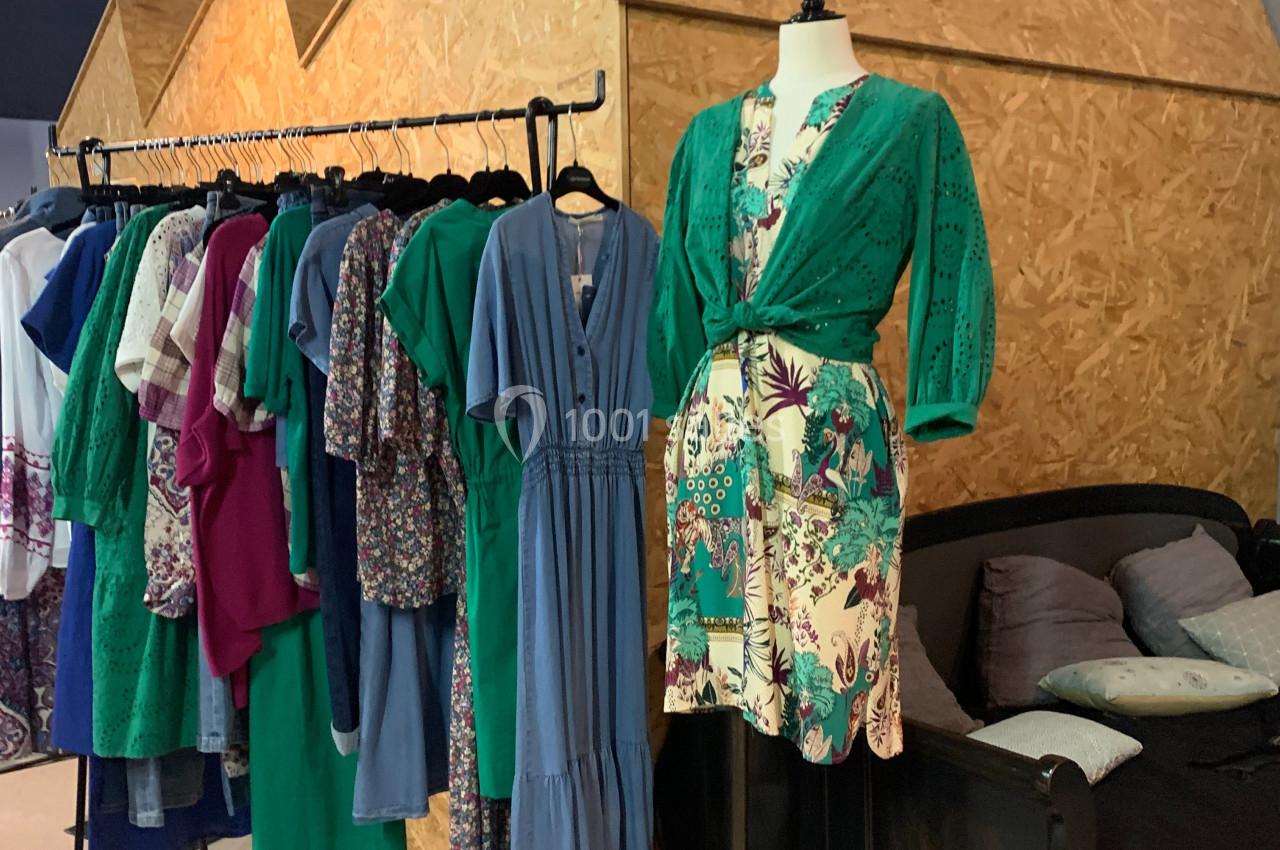 Portant de vêtements colorés à côté d'un mannequin habillé d'une robe verte et imprimée, dans un espace intérieur.