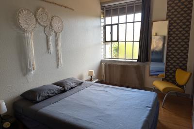 Salle lumineuse avec de grandes tables en bois dressées, chaises noires, décor minimaliste et verrière en hauteur.