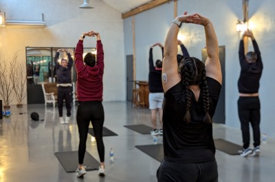 Salle lumineuse avec de grandes tables en bois dressées, chaises noires, décor minimaliste et verrière en hauteur.