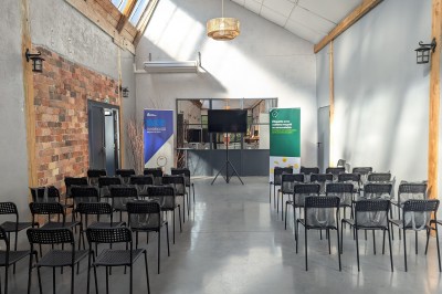 Salle lumineuse avec de grandes tables en bois dressées, chaises noires, décor minimaliste et verrière en hauteur.