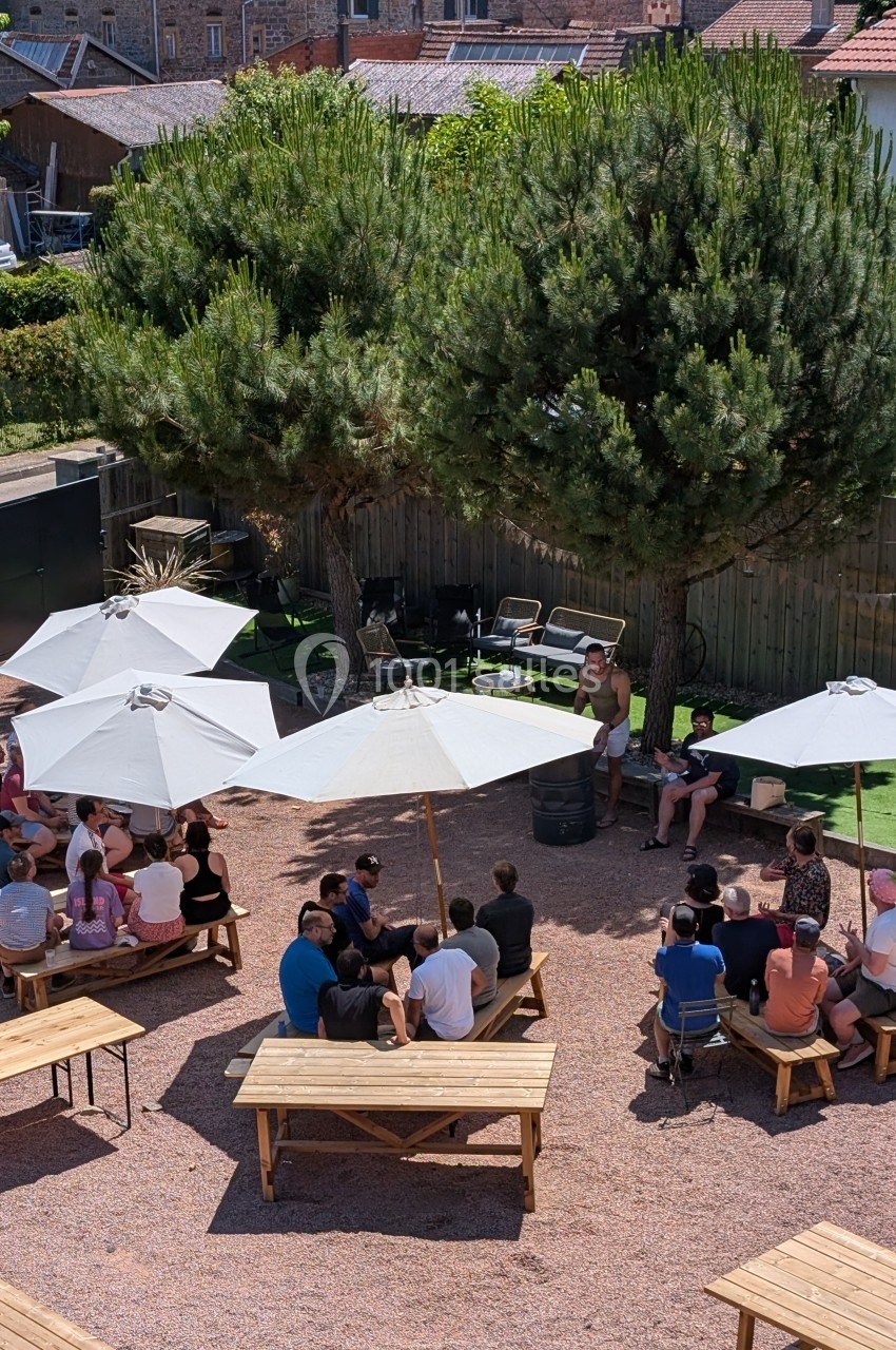 Groupe de personnes assises à des tables en extérieur sous des parasols, entourées d'arbres et de bâtiments.
